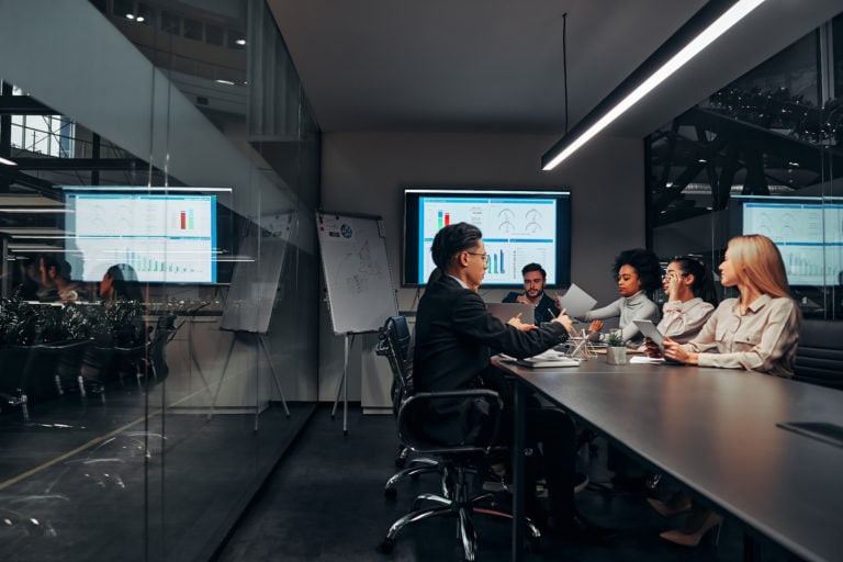 Work team. A group of successful business people work hard in the conference room of a large spacious office. In the room there is a monitor with graphs and a flipchart with a plan.